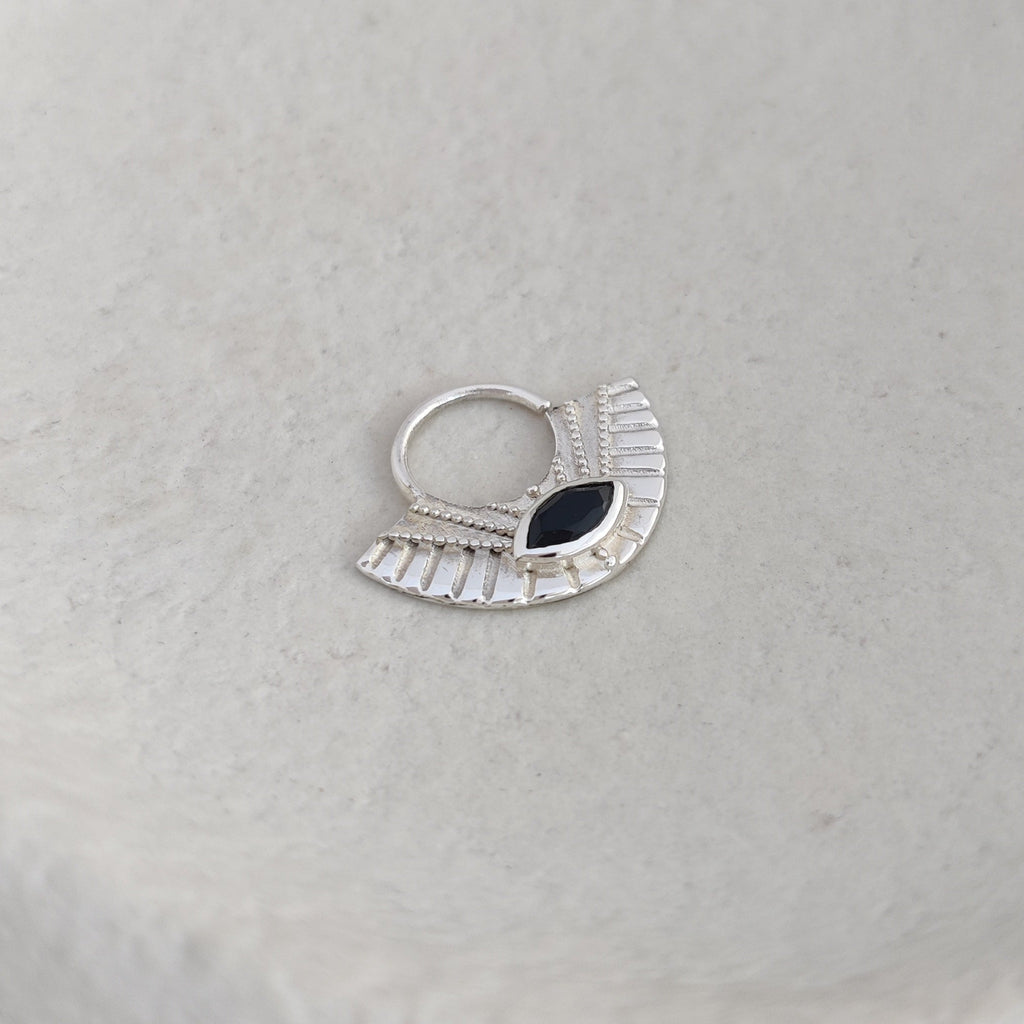 Silver septum nose ring with a black gemstone on a textured white surface