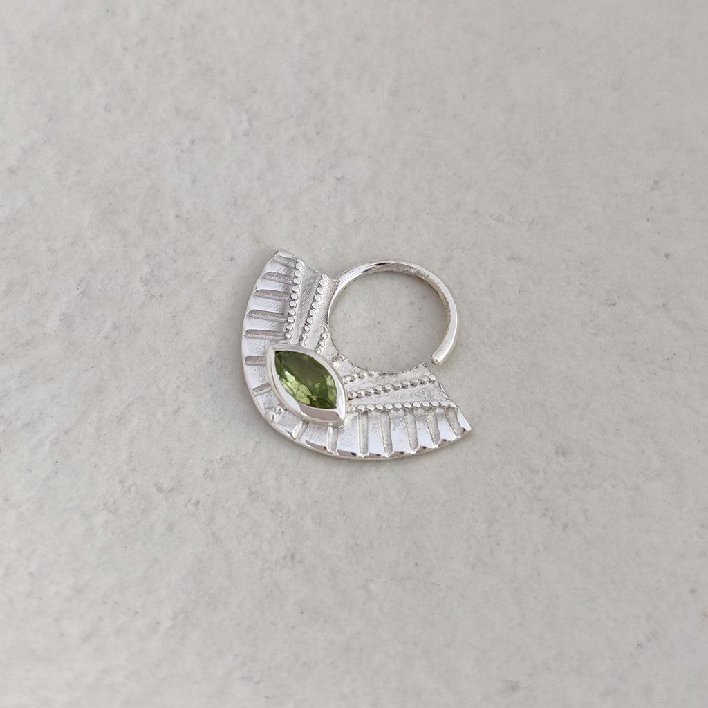 Silver septum nose ring with a green stone on a textured white surface.
