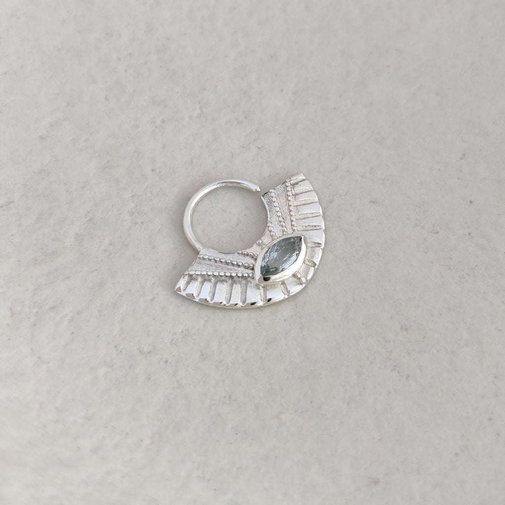 Silver septum nose ring with a blue topaz gemstone on a white background