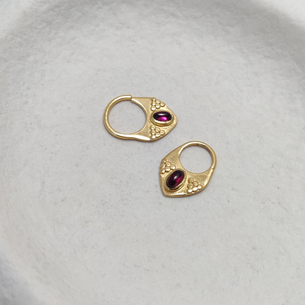 Close-up of gold septum nose rings with garnet showcased from various angles, highlighting their intricate design and v-shape design.