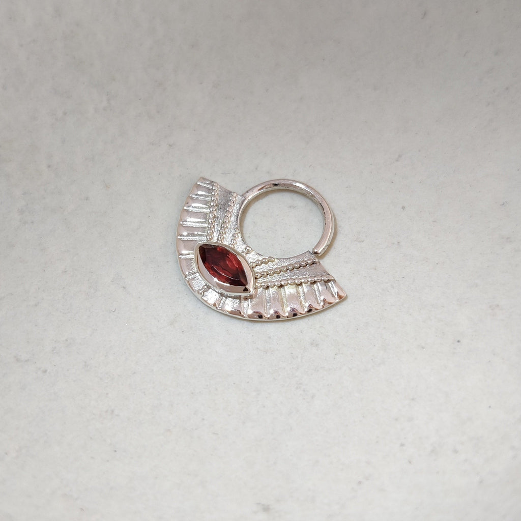Silver septum nose ring with a red gemstone on a white background