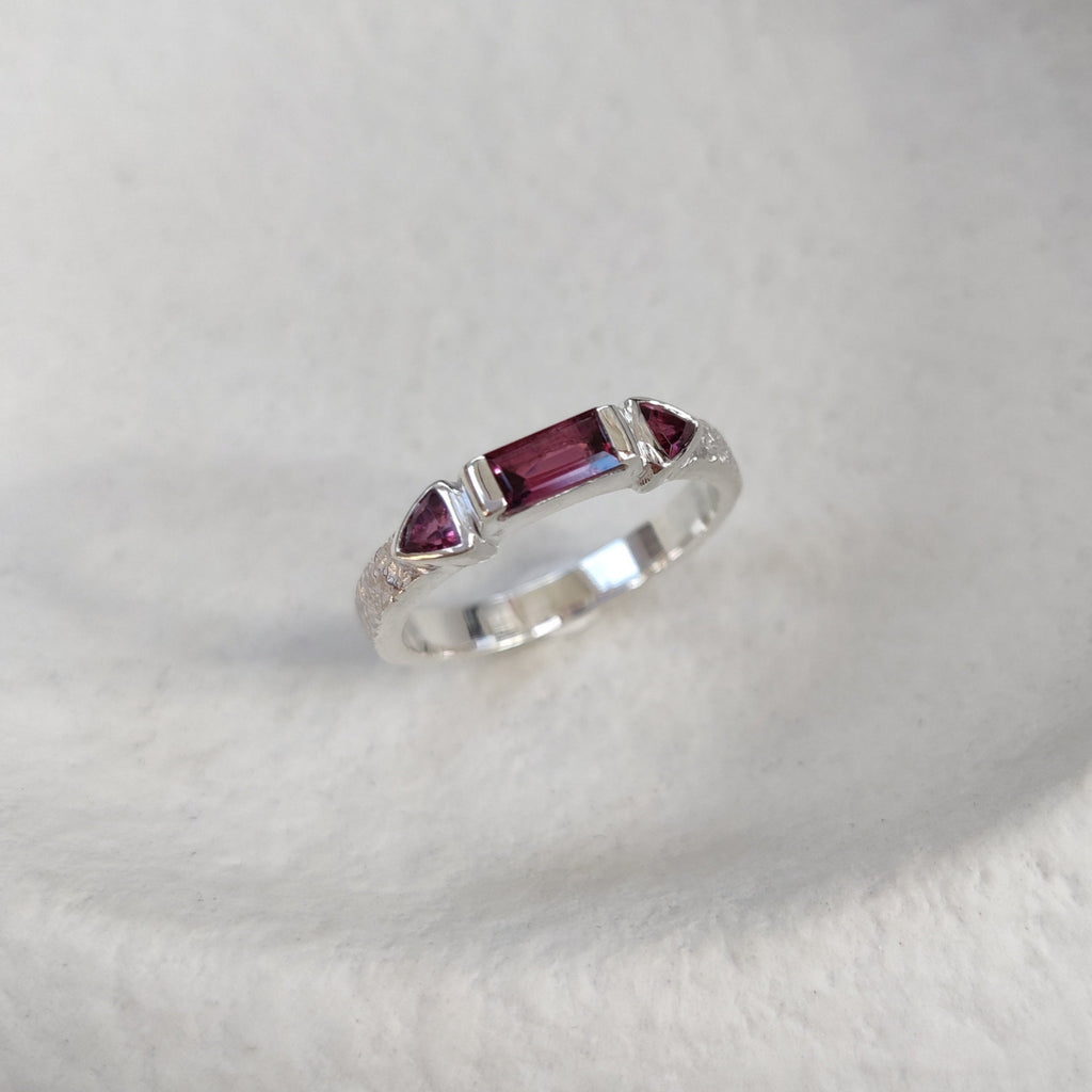 Silver ring with pink-purple gemstones on a white surface.