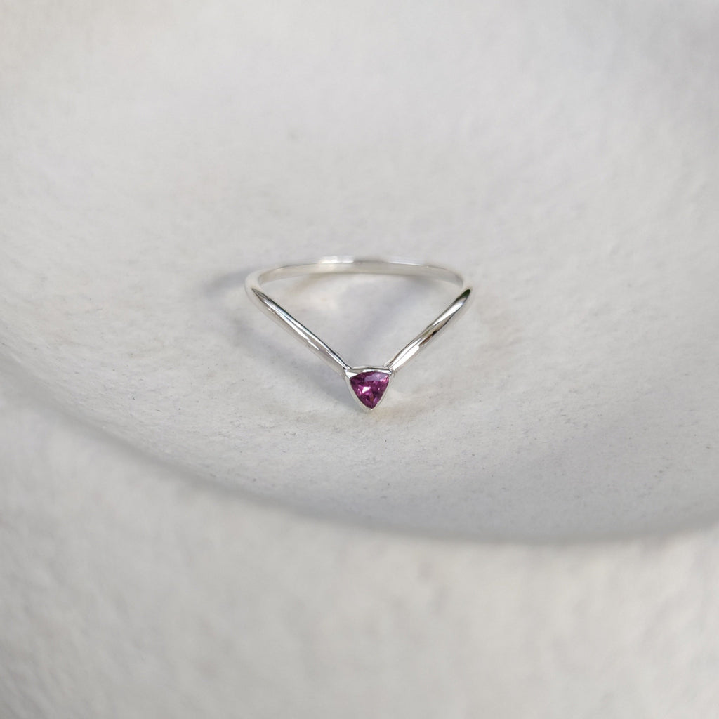 Dainty silver ring with a purple gemstone on a textured surface