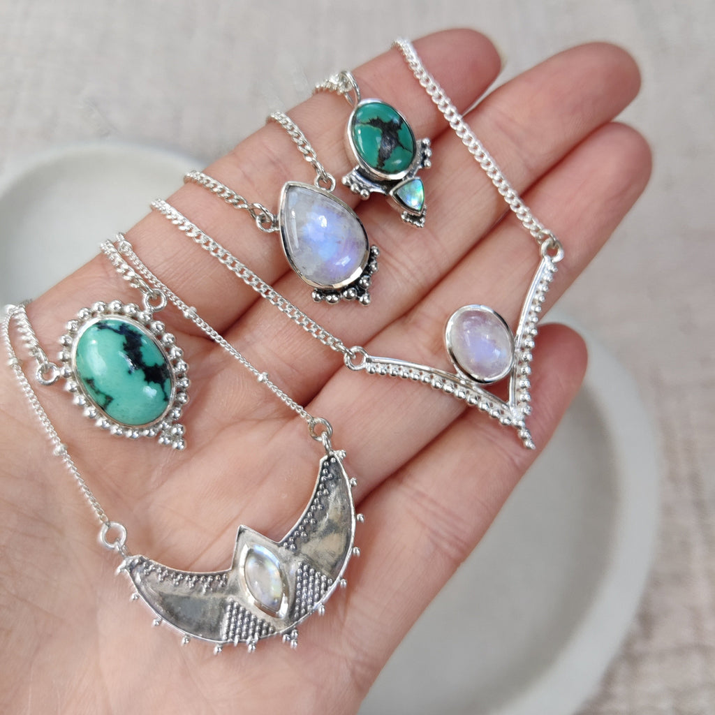 Hand holding silver necklaces with natural gemstone pendants on a light background.