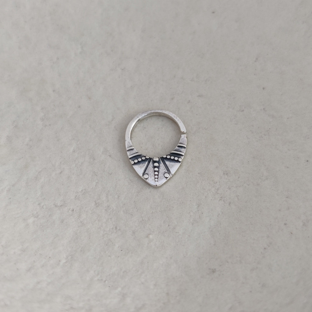 Silver nose ring with geometric design on a textured white surface.