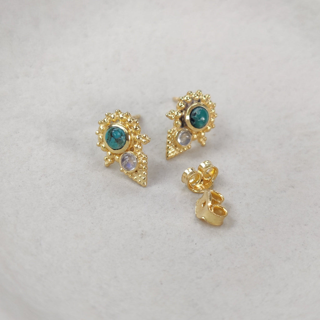 Gold earrings with turquoise and moonstone gemstones on a white plate