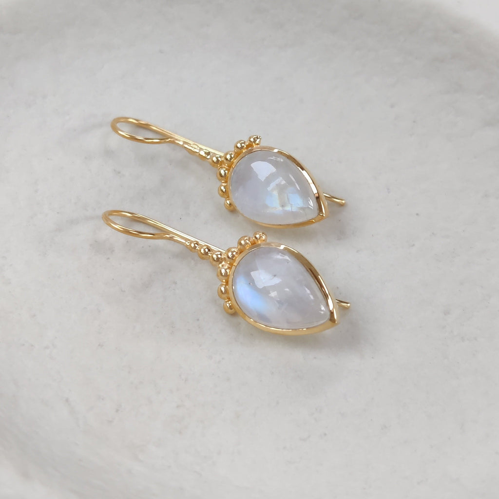 Gold earrings with moonstone stones on a white dish