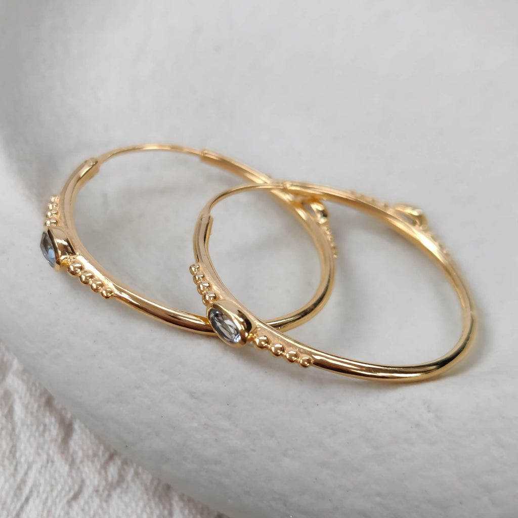 Gold hoop earrings with blue topaz on a textured white surface