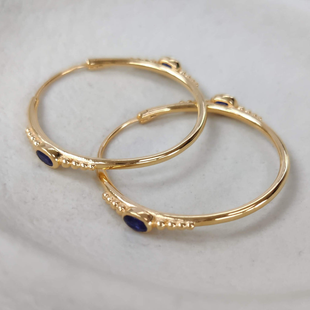 Gold hoop earrings with blue stones on a white surface