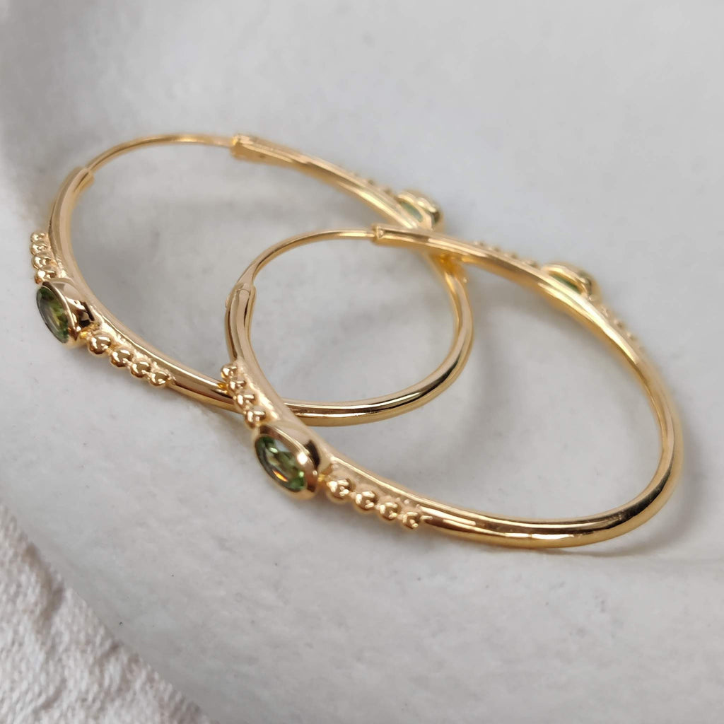 Textured gold hoop earrings with green gemstones on a textured white surface