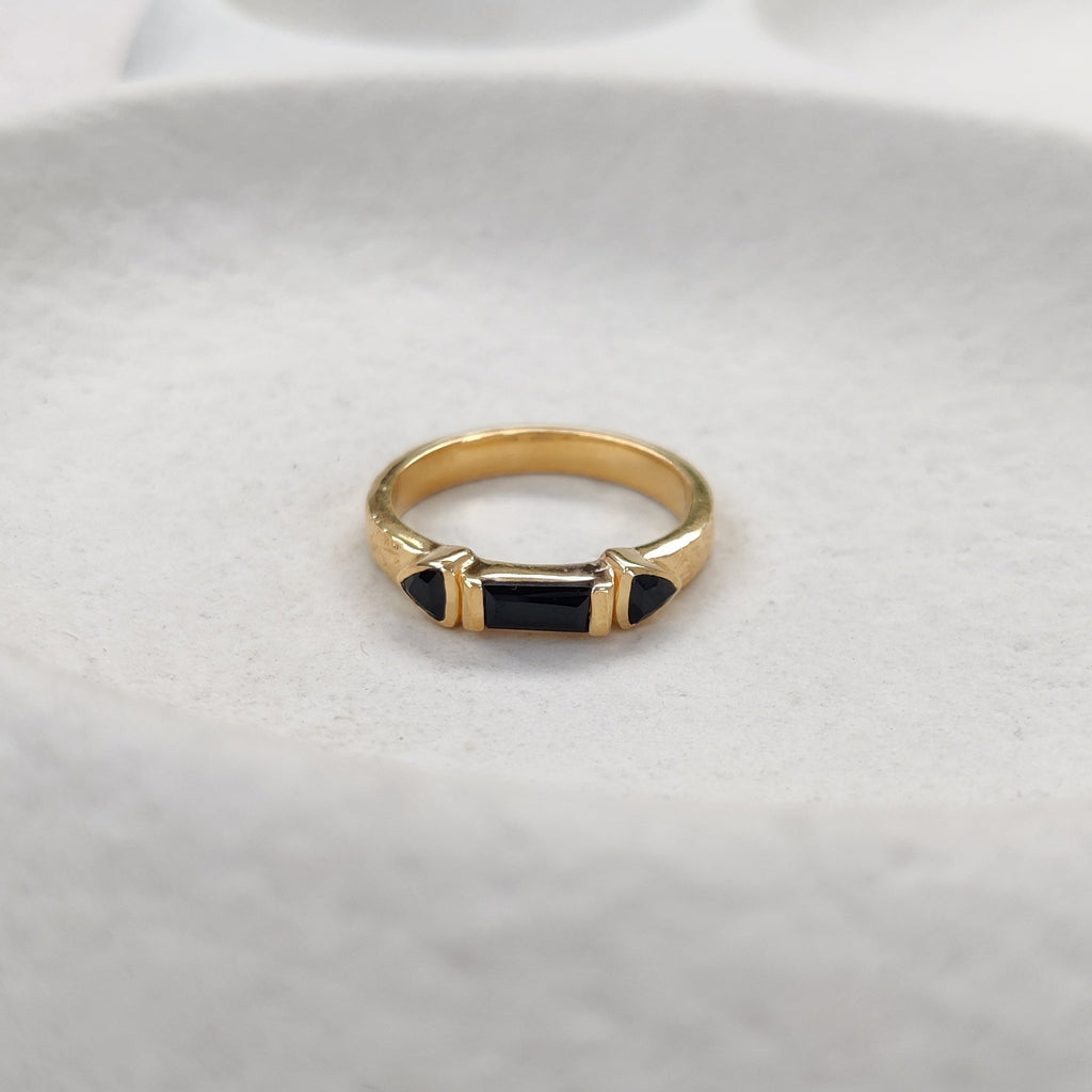 Gold ring with black onyx gemstones on a white ceramic dish