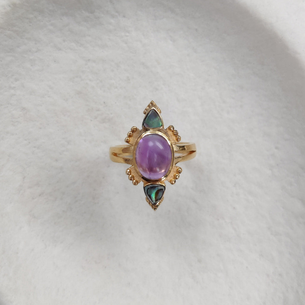 Gold ring with a purple gemstone on a white stone surface