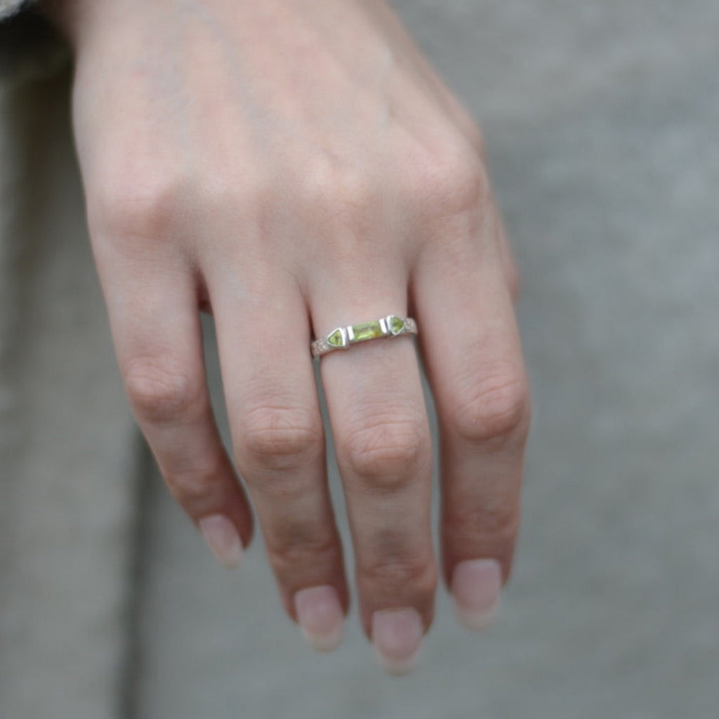Hand wearing a three stone gold ring on a neutral background