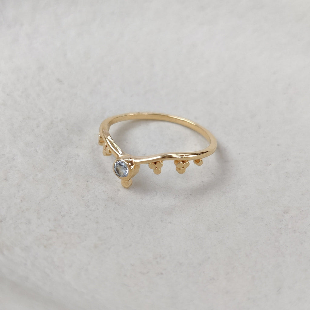 Gold ring with small blue topaz gemstone on a textured white surface.