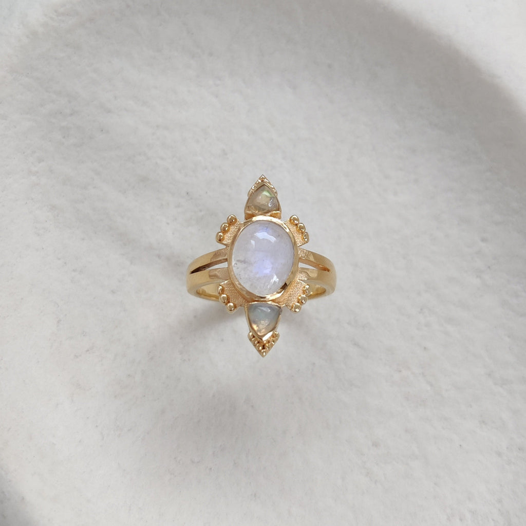Gold ring with moonstone and opals on a textured white surface.