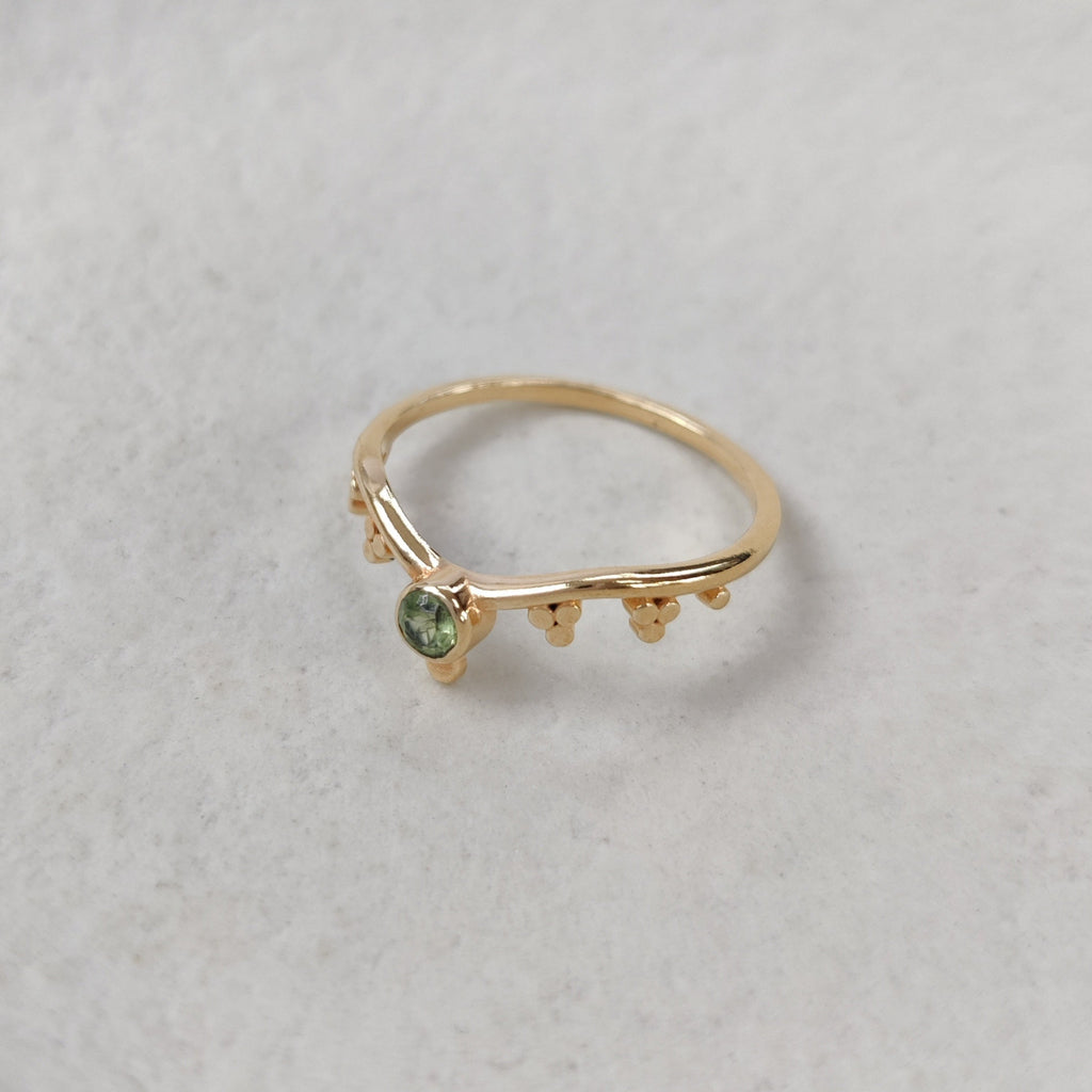 Dainty gold ring with a green gemstone on a white background.