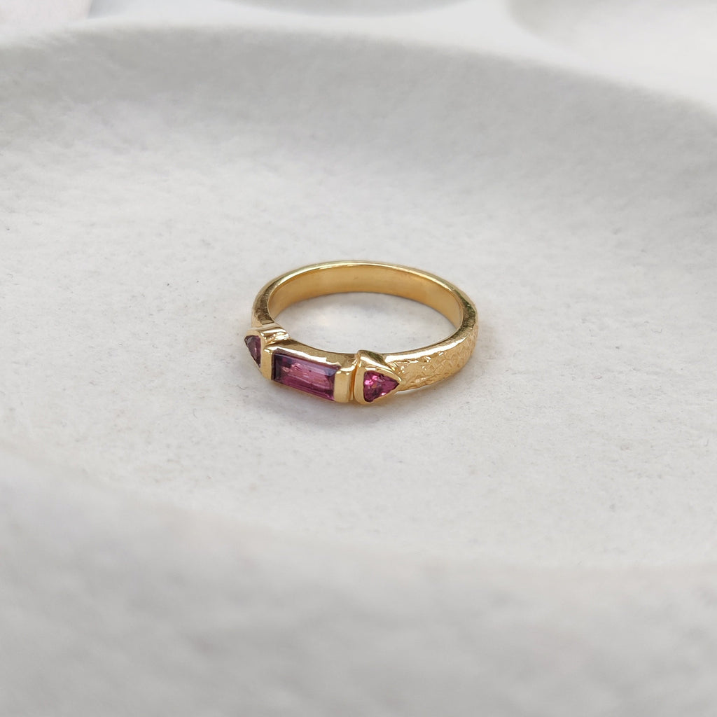 Gold ring with a purple gemstone on a white cushion