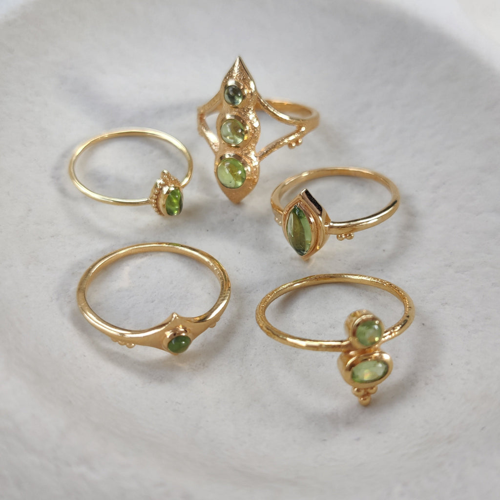 Set of gold rings with green gemstones on a white surface.