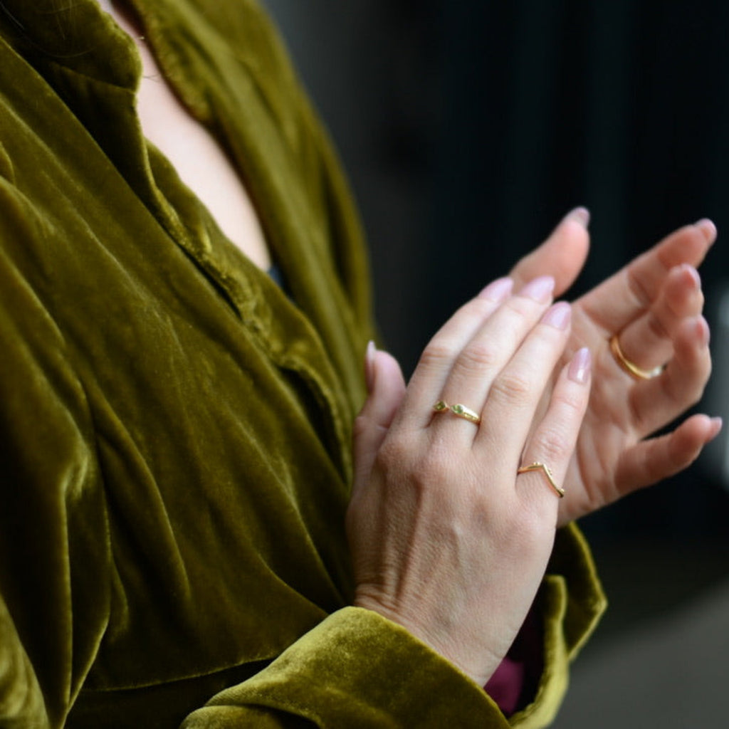 Person wearing a green velvet outfit with gold rings on fingers.