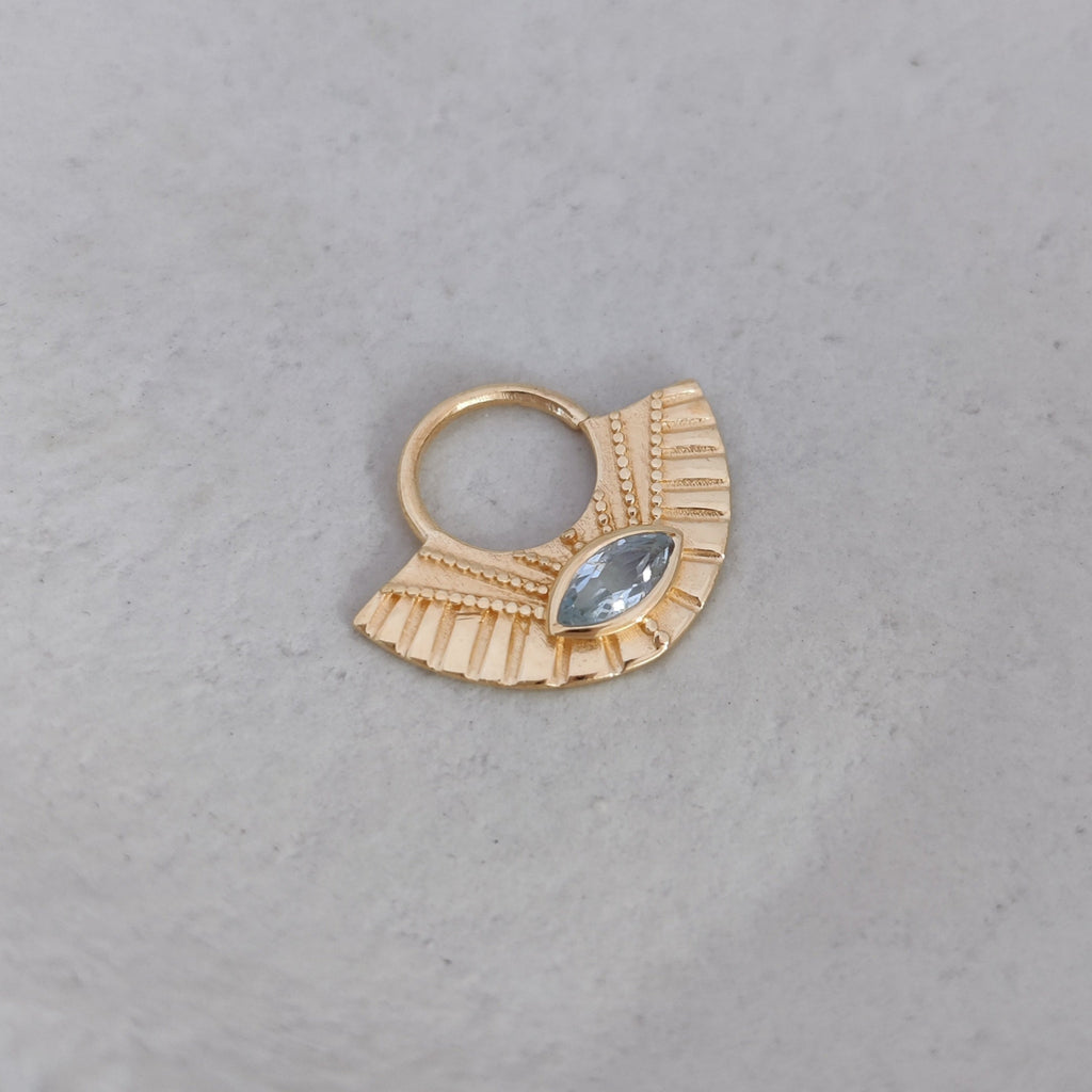 Gold septum nose ring with a blue topaz gemstone on a light background.