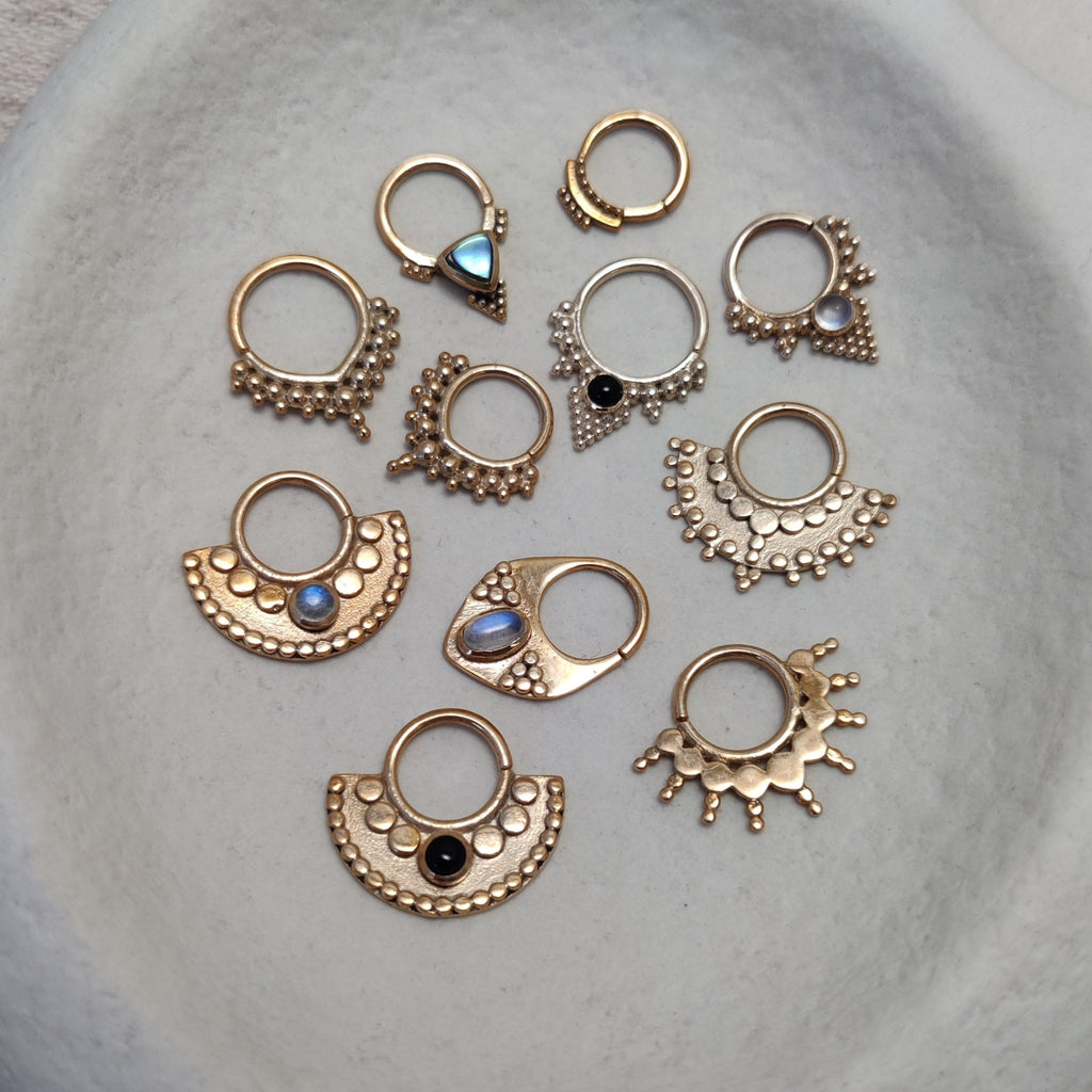 Collection of gold septum jewelry, displayed on a jewelry plate. Noomaad design.