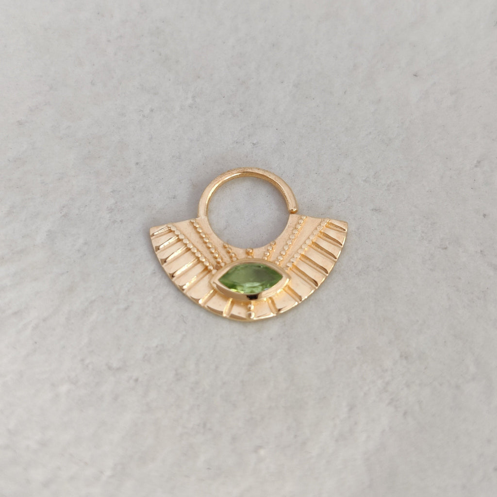 Gold septum nose ring with a green gemstone on a light background.