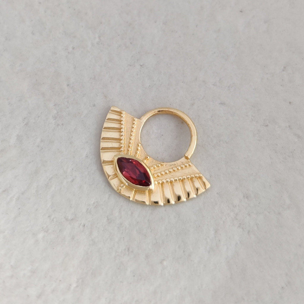 Gold septum nose ring with a red gemstone on a light background.