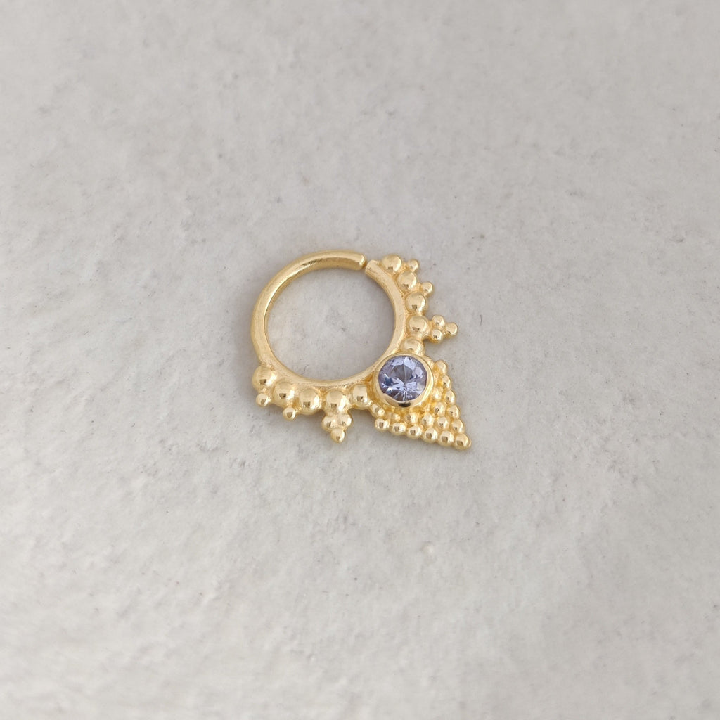 Gold septum ring with blue purple tanzanite gemstone on white background