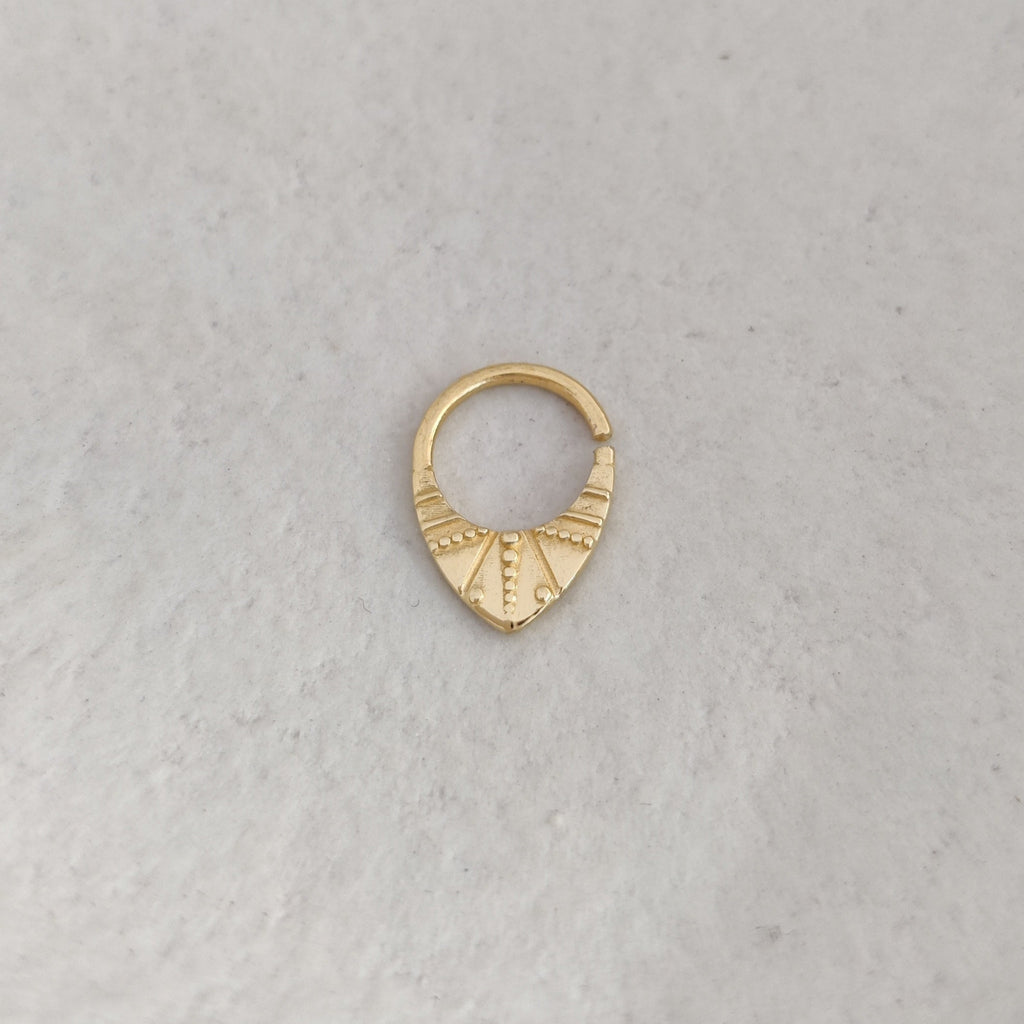 Gold septum nose ring on a light textured surface.