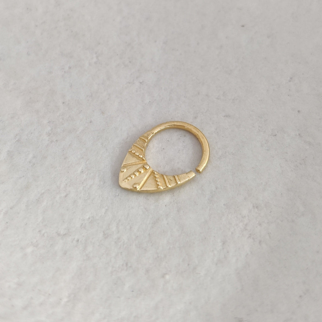 V-shaped gold septum ring on a textured white surface.