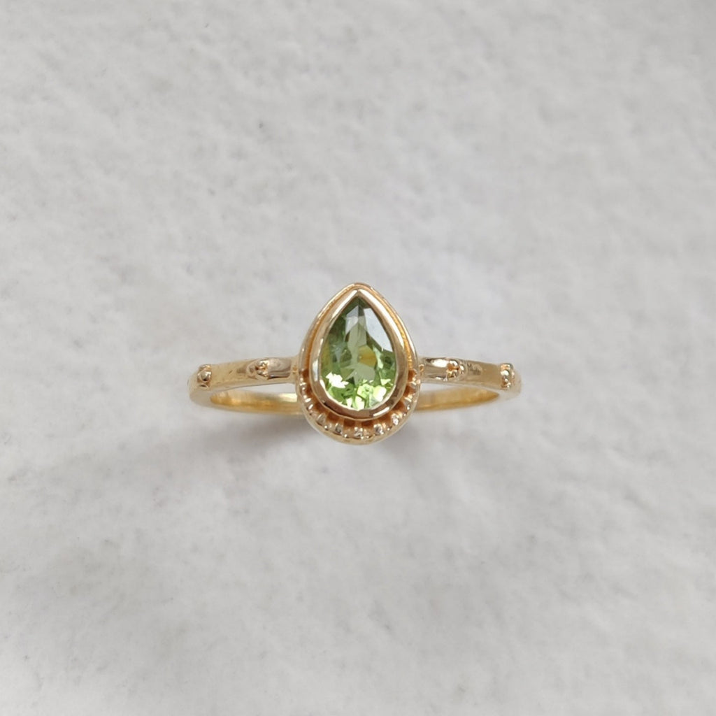 Gold ring with a green faceted gemstone on a white background.