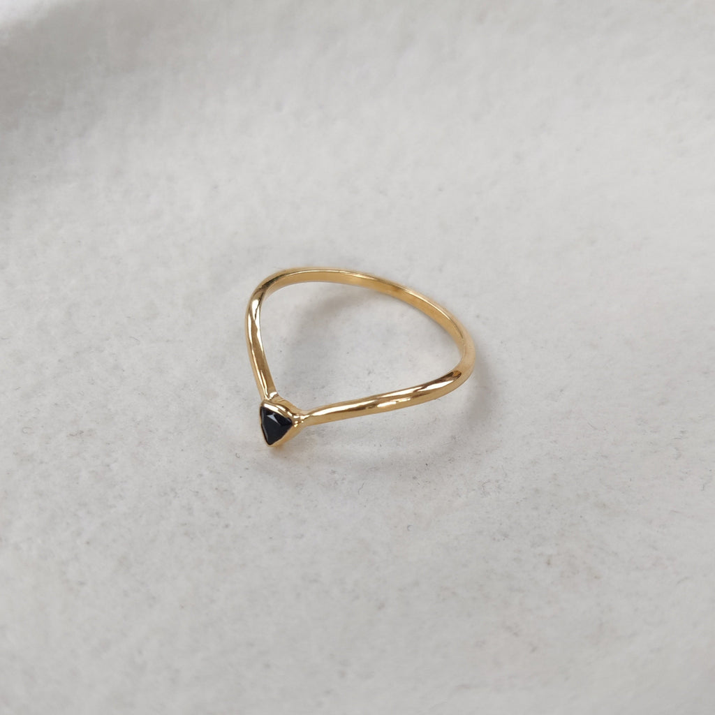 V-shaped gold stacking ring with a trillion-shaped black gemstone on a light background