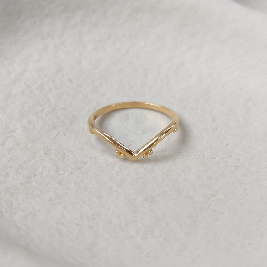 Chevron gold ring on a textured white surface.