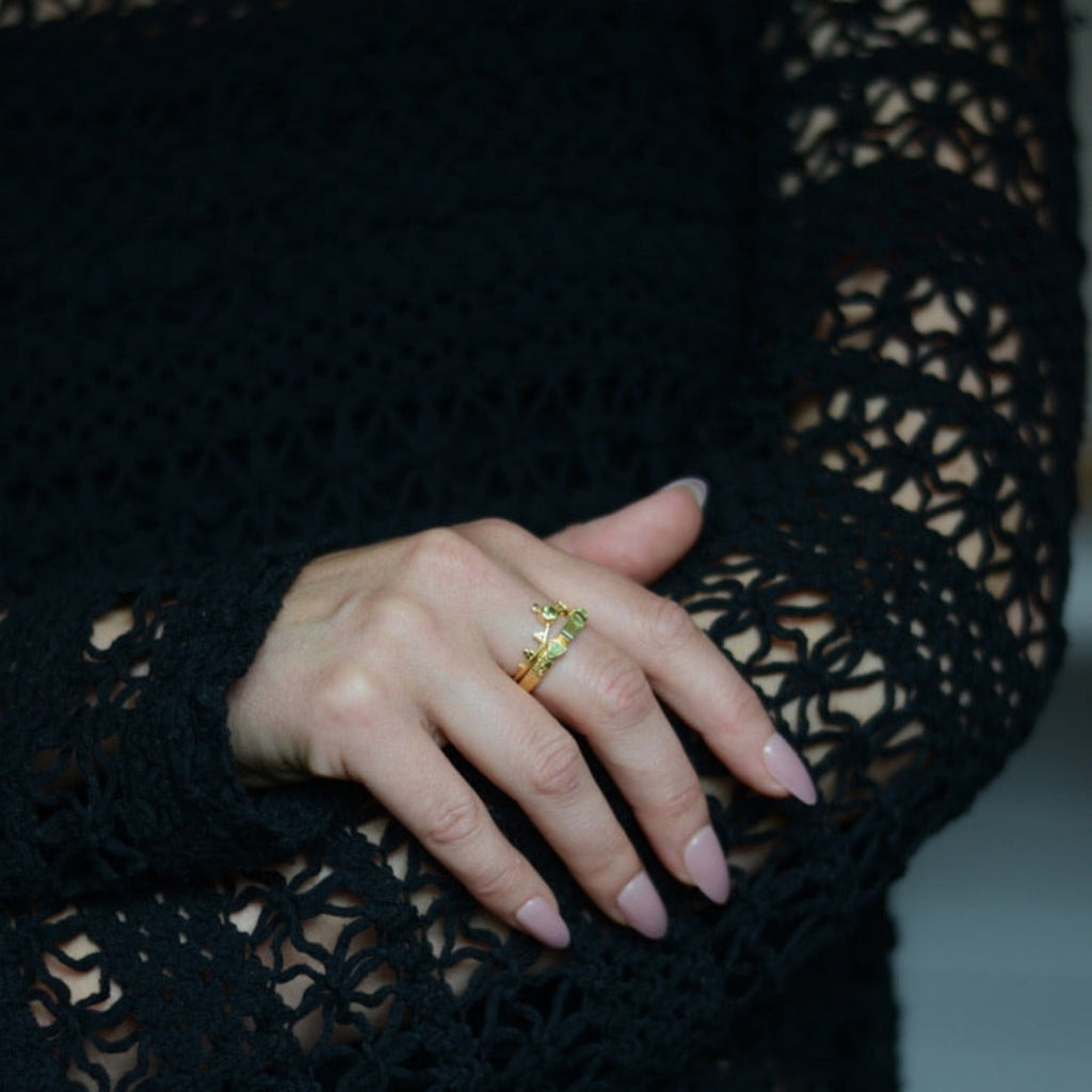 Close-up of a hand wearing gold stacking rings with peridot gemstones on a black crocheted garment.