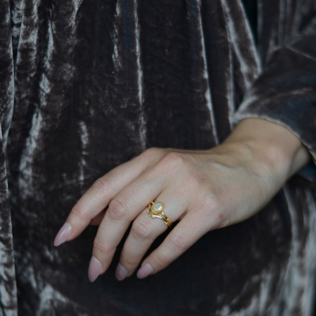 Hand wearing two gold stacking rings with a drop-shaped moonstone.