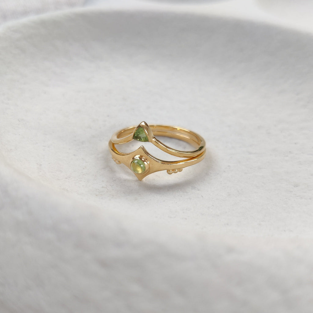 Gold stacking rings with a green gemstones on a white stone surface.