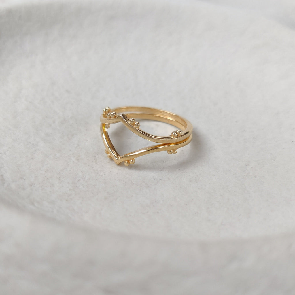 Two gold stacking rings on a textured white surface.