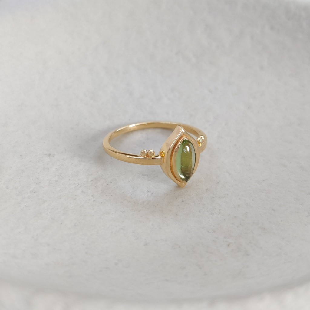 Gold ring with a green gemstone on a textured white surface.