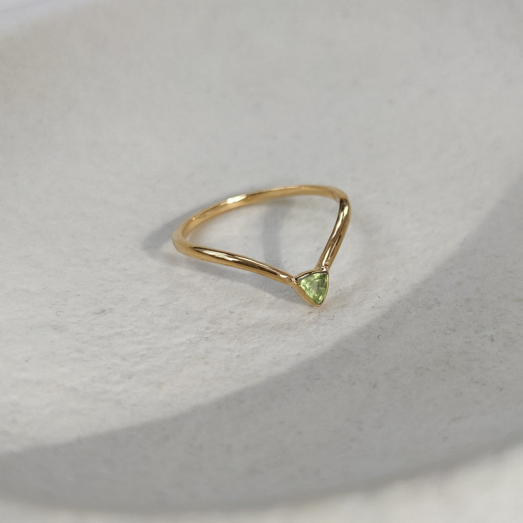 V-shaped gold ring with a green gemstone on a light surface