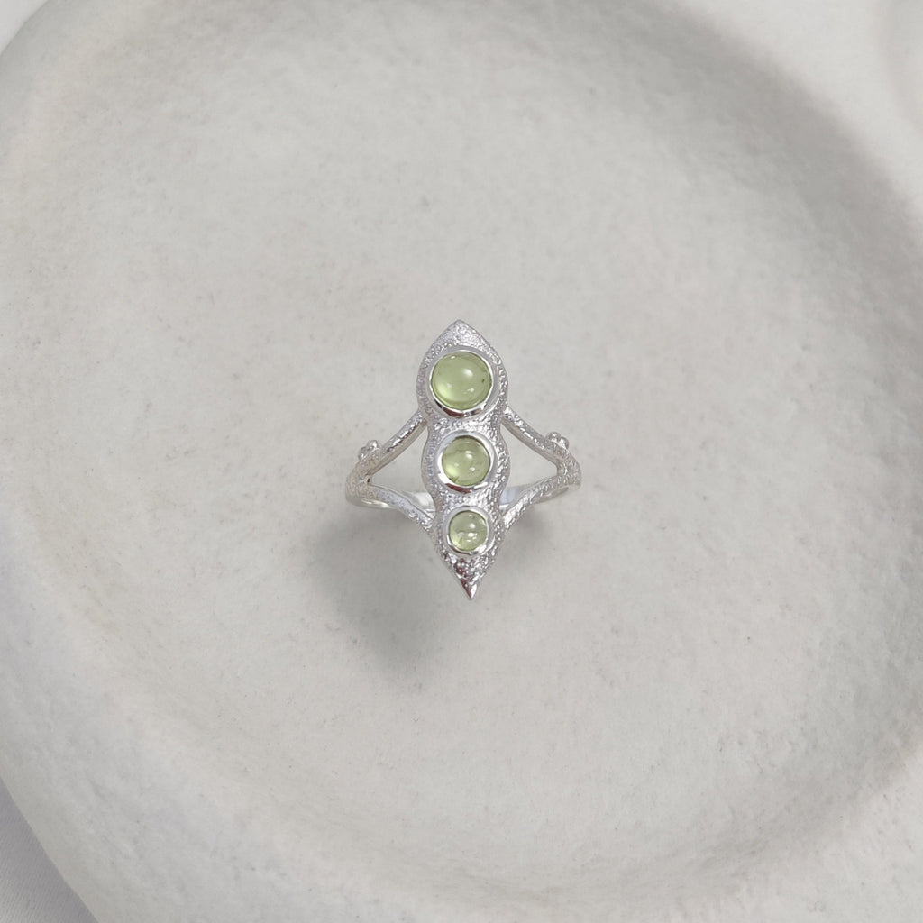 Silver ring with green gemstones on a white surface.