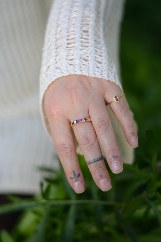 Hand with multiple gold rings with rhodolite garnet on a blurred green background