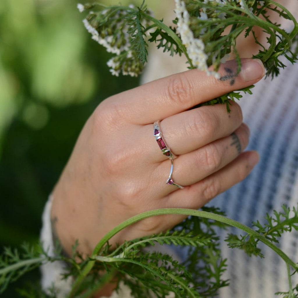 Hand with silver and rhodolite garnet rings holding green leaves with a blurred natural background
