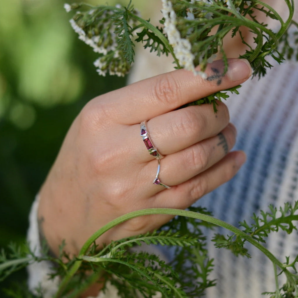 Hand with silver and rhodolite garnet rings holding green leaves with a blurred natural background