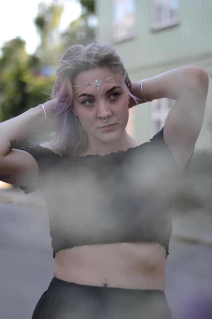 Person with purple hair, moonstone head chain and a nose ring standing outdoors with blurred background