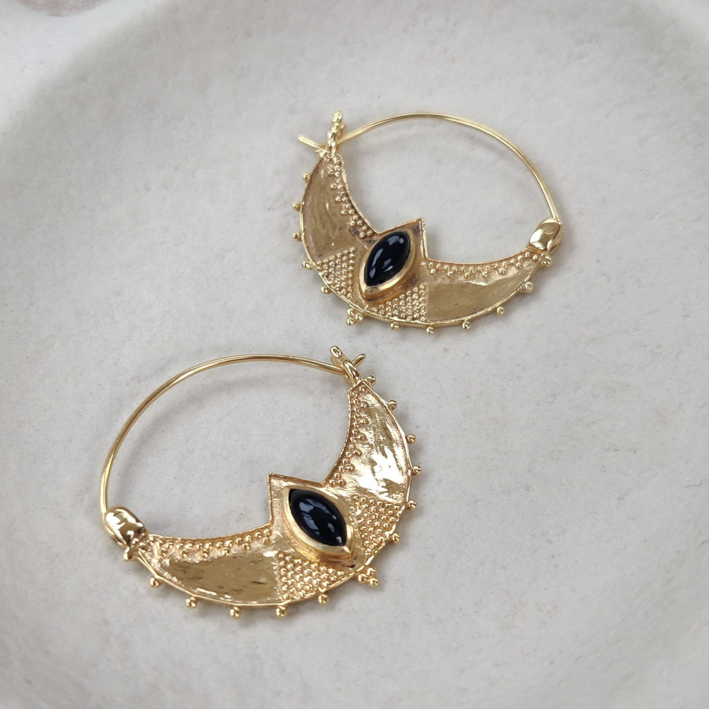 Gold hoop earrings with black gemstones on a white dish.