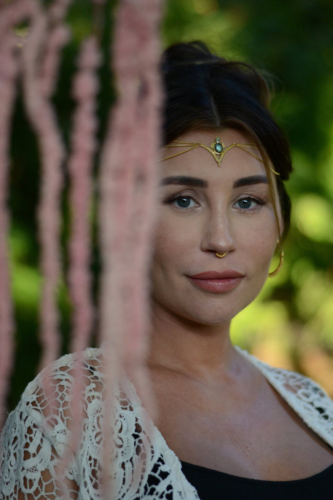 A model wearing a gold and gemstone head chain with a v-shaped design and three chains draping on each side.