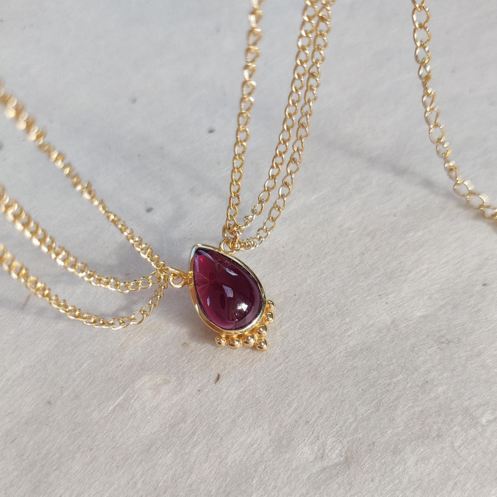 Gold head chain with drop-shaped red gemstone centerpiece, and three chains draping on each side.