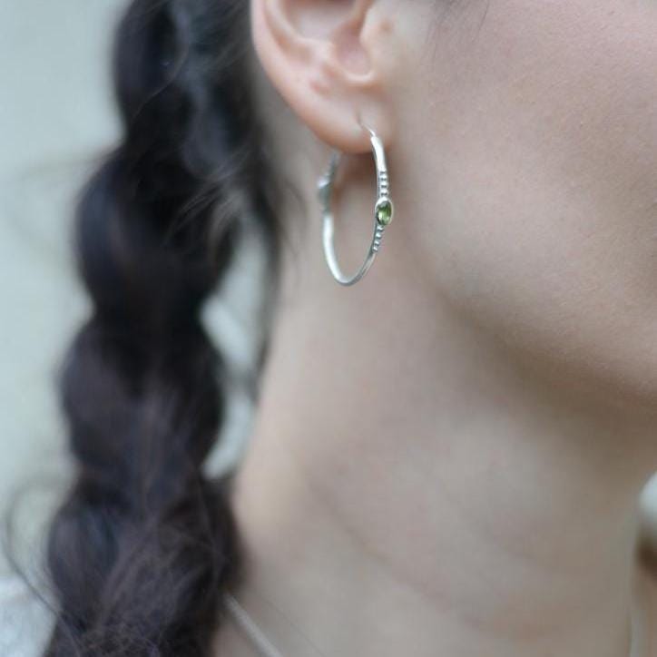 Bohemian silver hoop earrings with faceted green gemstones worn on a model.