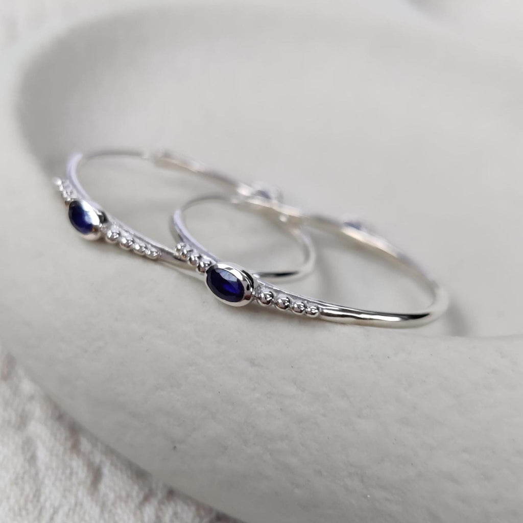 Bohemian silver hoop earrings with faceted dark blue sapphires on a white surface.