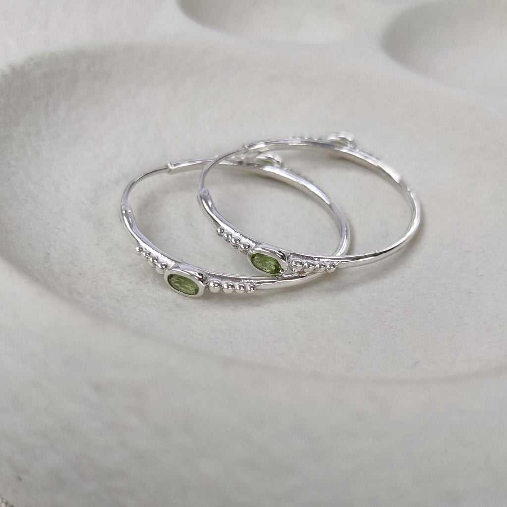 Bohemian silver hoop earrings with faceted green gemstones on a white surface.